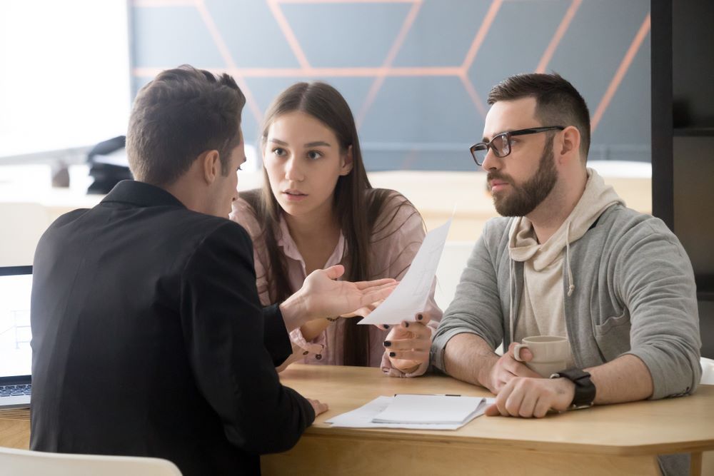 A Man and a Woman Are Sitting at a Table Talking to Each Other — All About Conveyancing Taree In Taree, NSW
