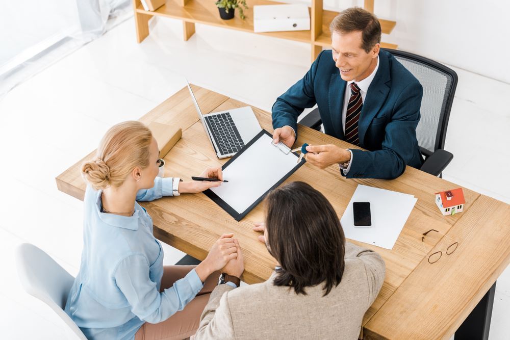 A Man in a Suit and Tie is Sitting at a Table With Two Women — All About Conveyancing Taree In Taree, NSW