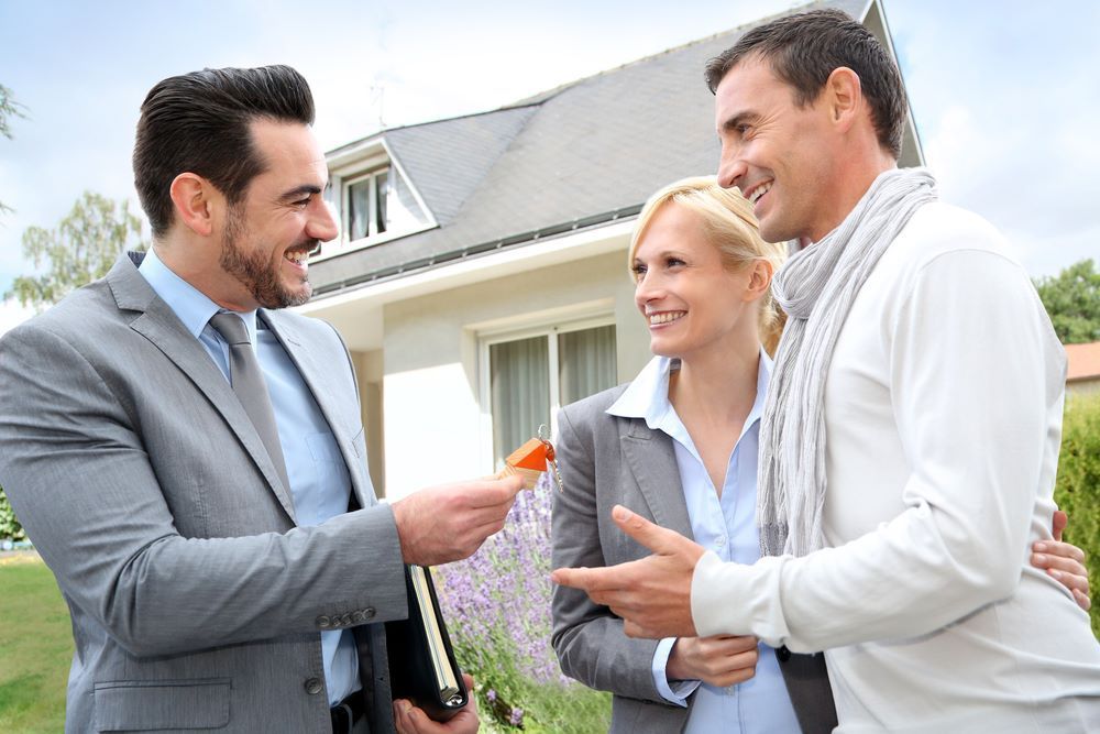 A Man is Giving a Key to a Woman and a Man in Front of a House — All About Conveyancing Taree In Taree, NSW