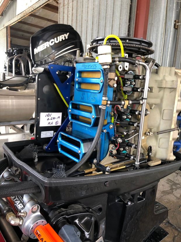 Boat motor with spark plug wires, various hoses and wires, outdoors.