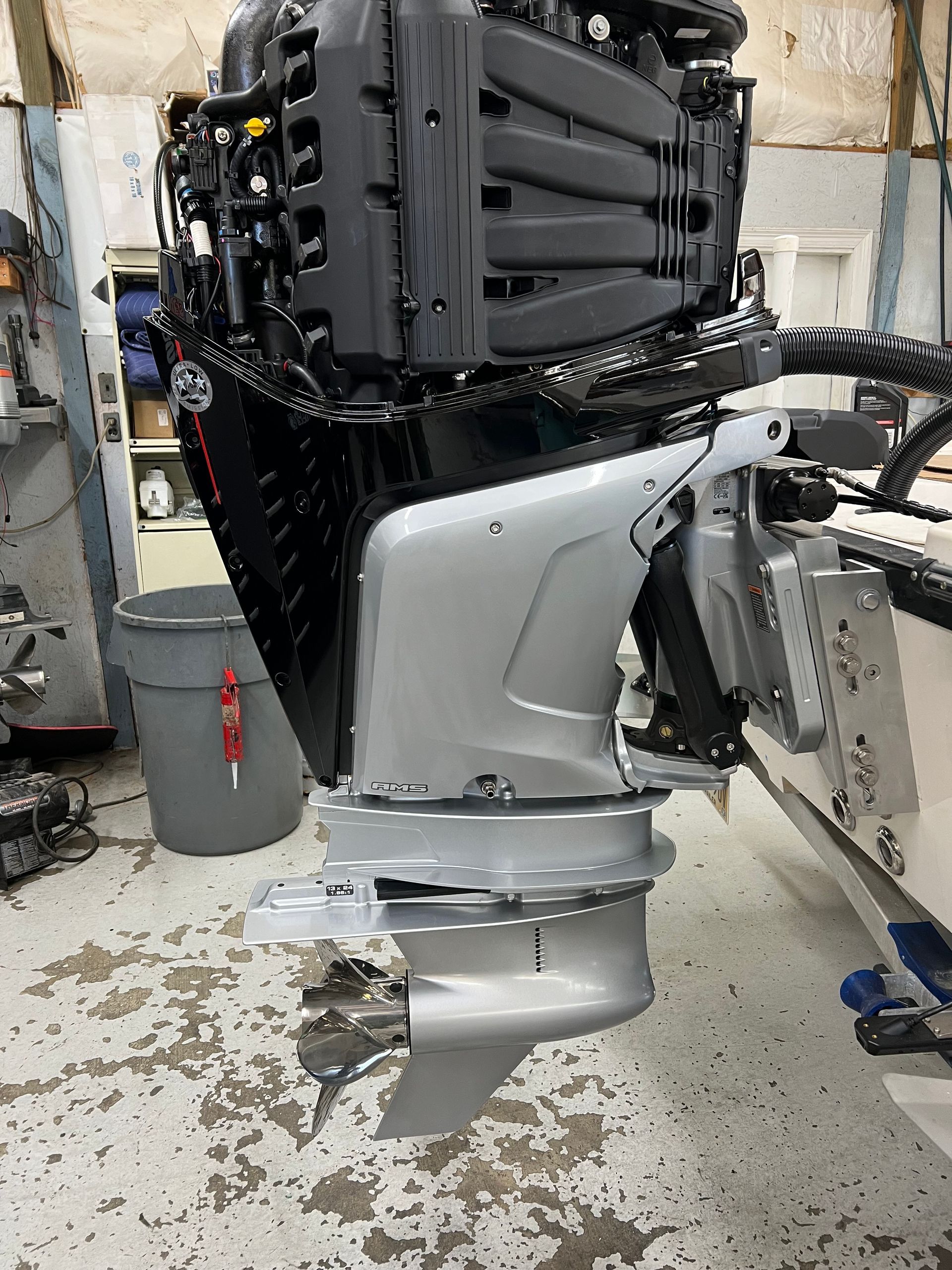 Outboard boat motor, silver and black, mounted on a boat in a workshop.