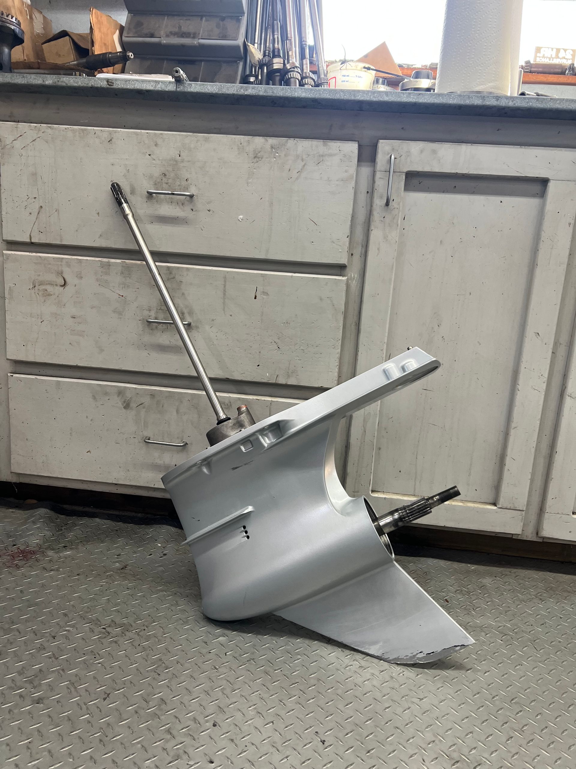 Gray outboard motor lower unit, angled against a cabinet with drawers, in a workshop setting.