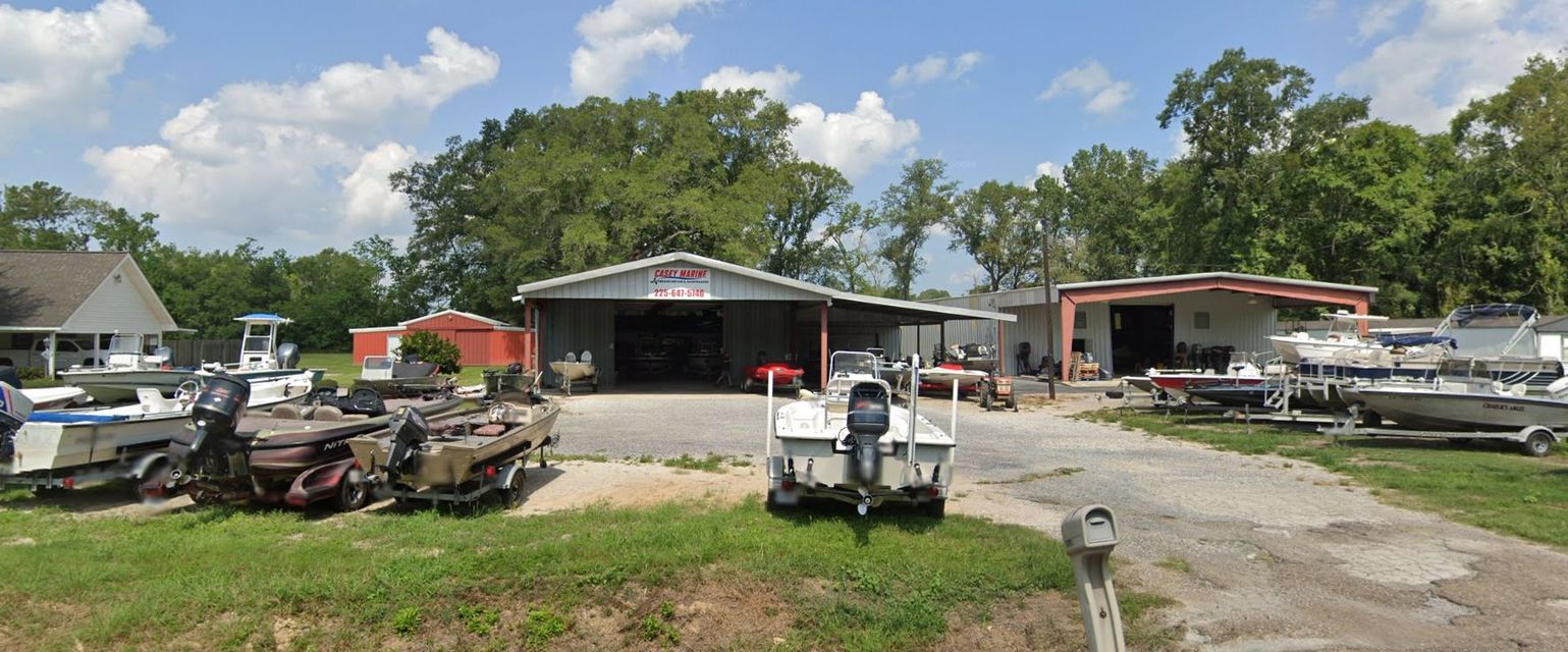 Boats parked in front of a boat repair shop, under a blue sky, with trees in the background.
