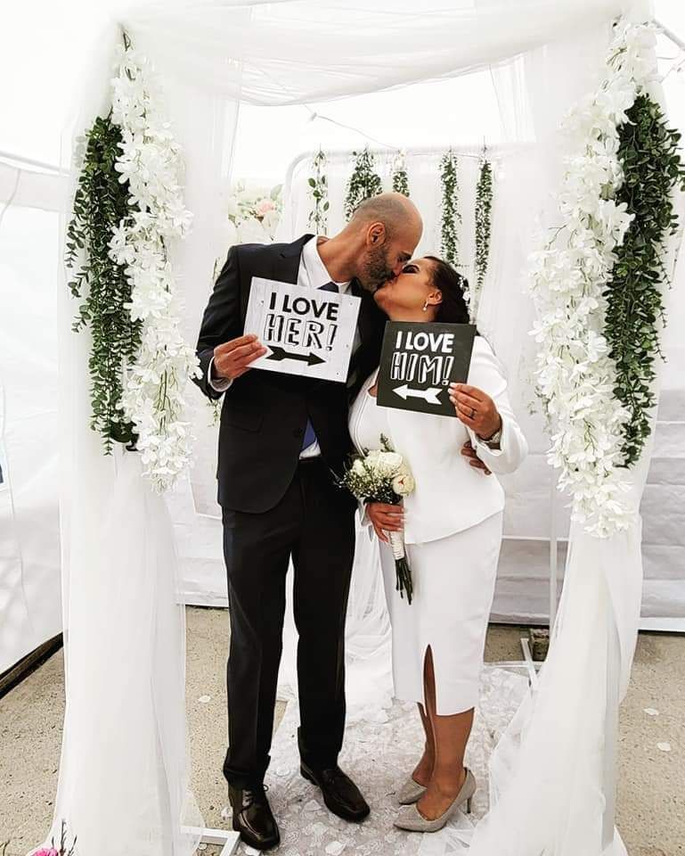 Three people pose for a photo at a wedding; balloons and flowers decorate the ceremony space.