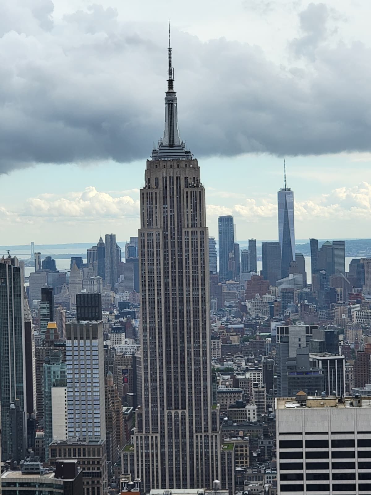 The Empire State Building rises prominently in the center of the New York City skyline under a cloudy sky.