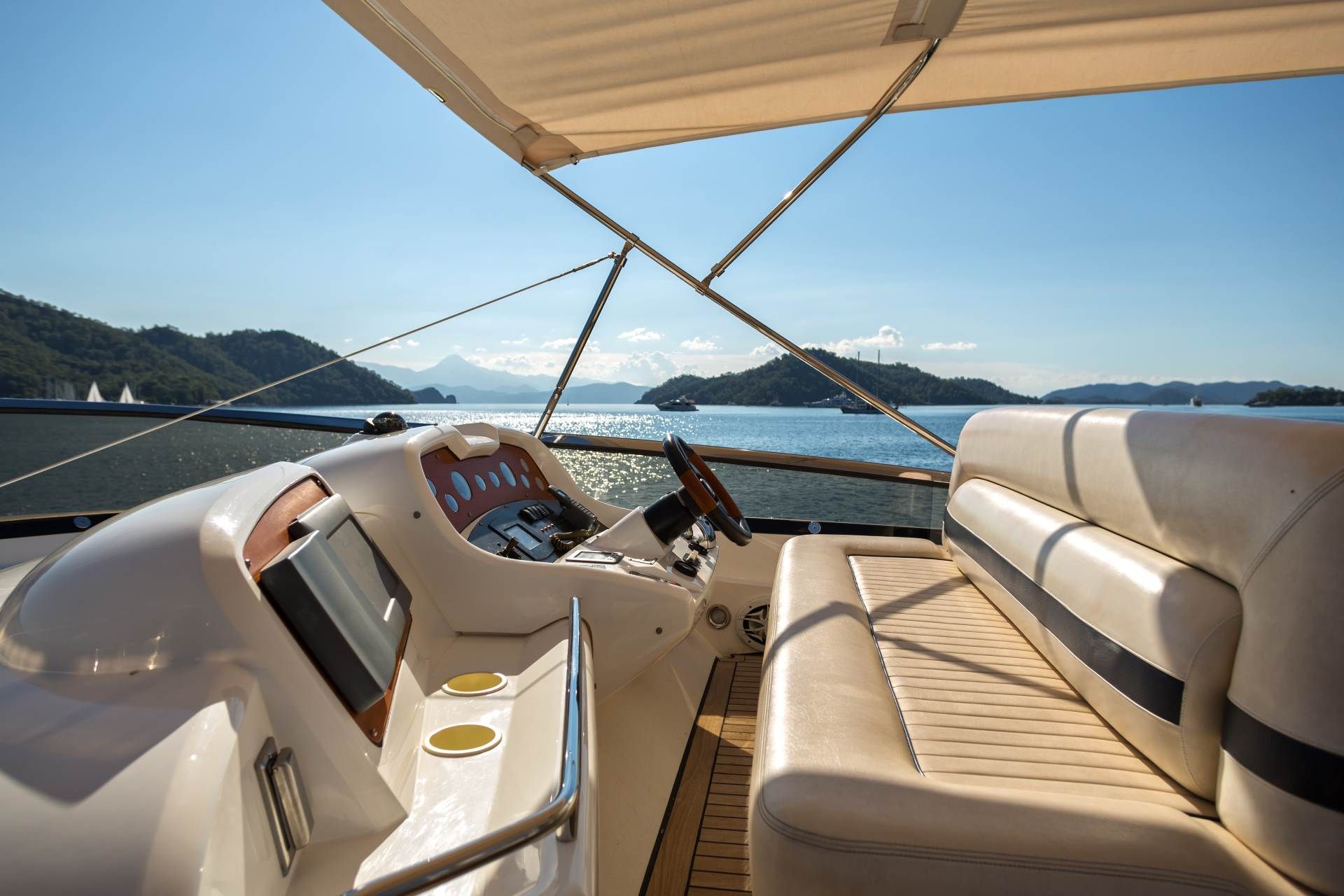Boat deck with beige seating and canopy overlooking calm water and distant islands at sunset