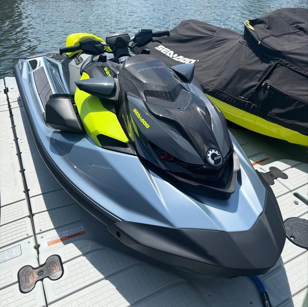 Blue and black Sea-Doo jet ski on a dock with a black cover and water in the background.