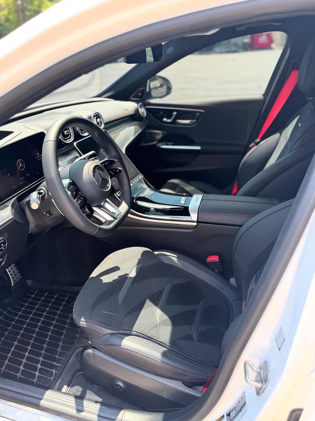 Interior view of a white Mercedes-Benz. Black seats with red seatbelts and steering wheel. Black dashboard and checkered floor mats.