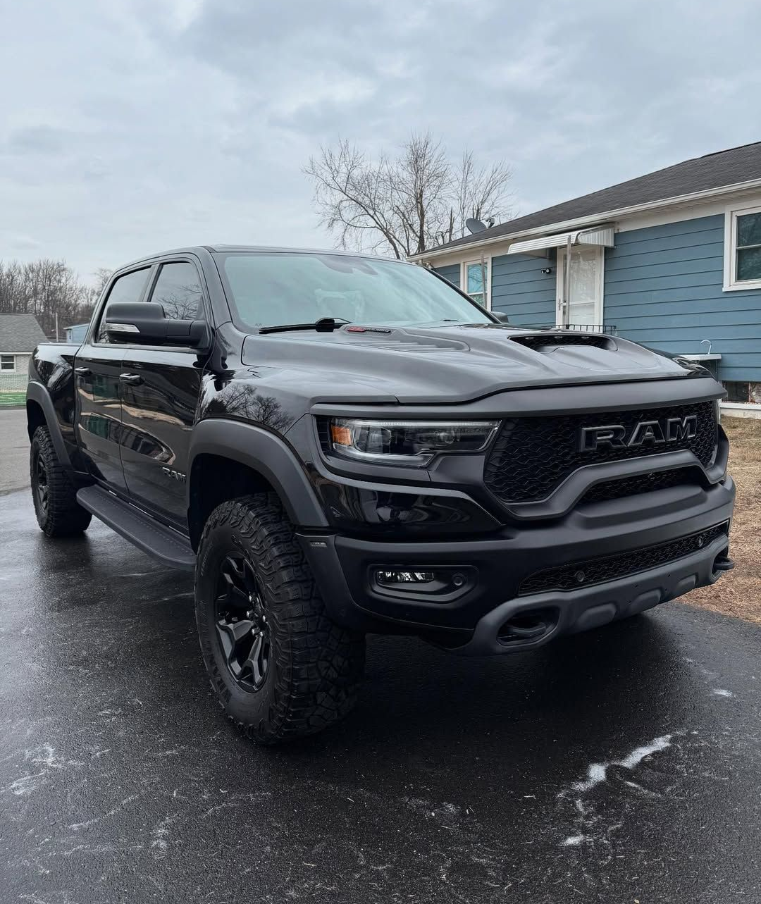 Black Ram TRX truck parked on a wet driveway in front of a blue house.