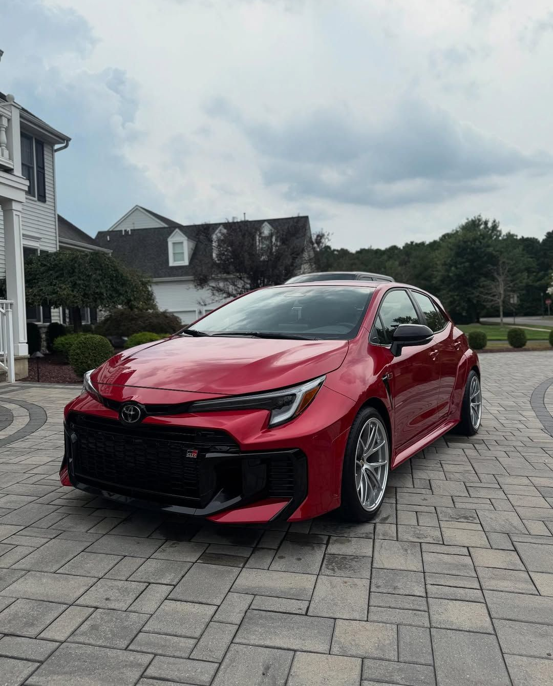 Red Toyota Corolla hatchback parked on a brick driveway in front of a house.