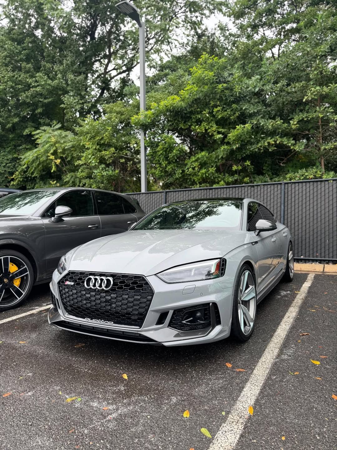 Silver Audi RS5 parked in a lot, black grille, next to another car.