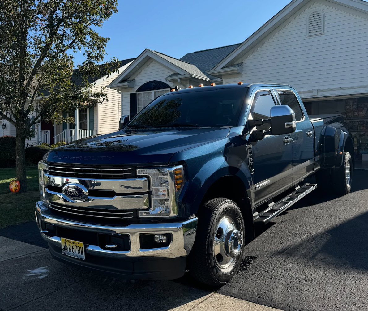 Blue Ford pickup truck parked on a driveway in front of a house on a sunny day.