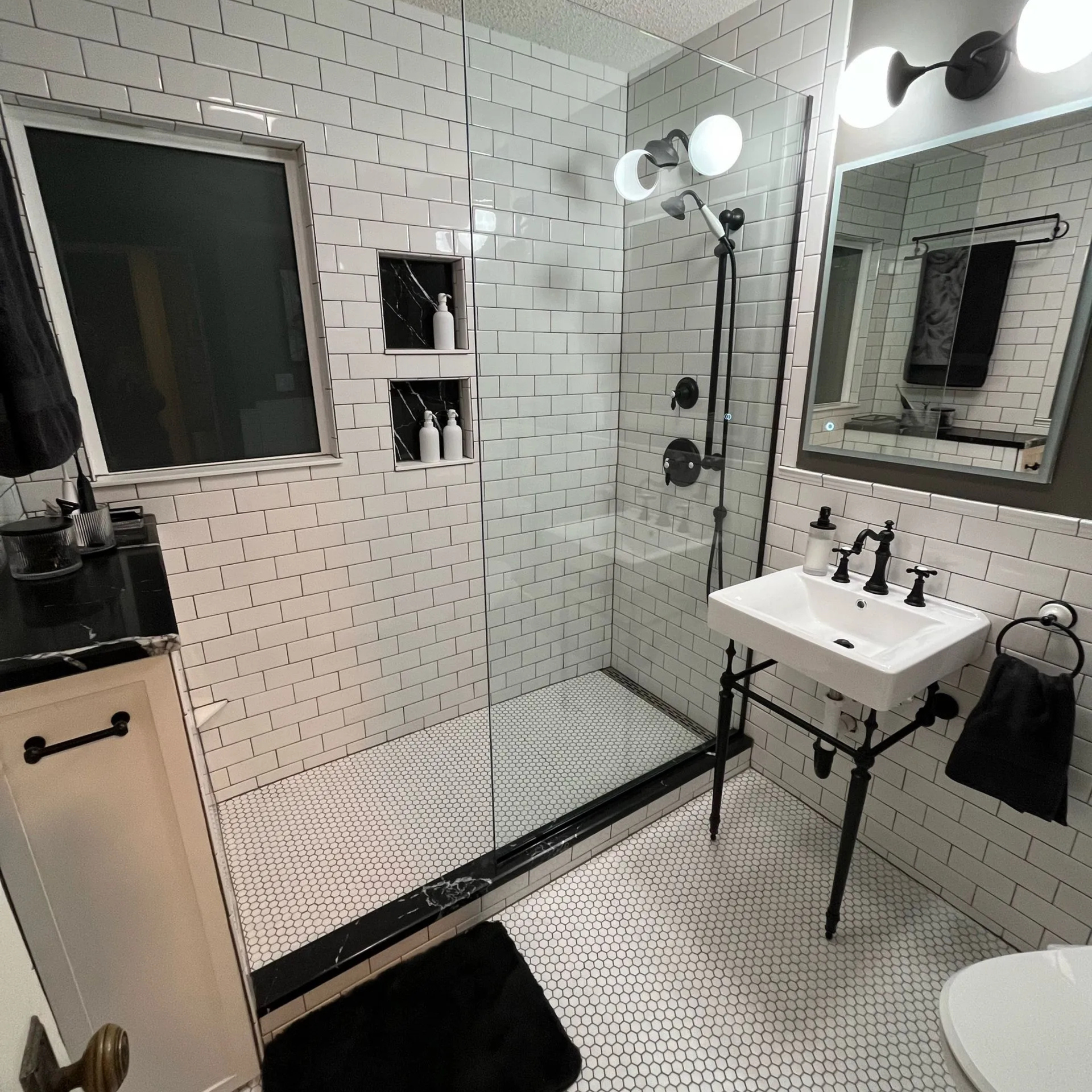 Modern bathroom with gray tile, toilet, sink, and window with blinds.