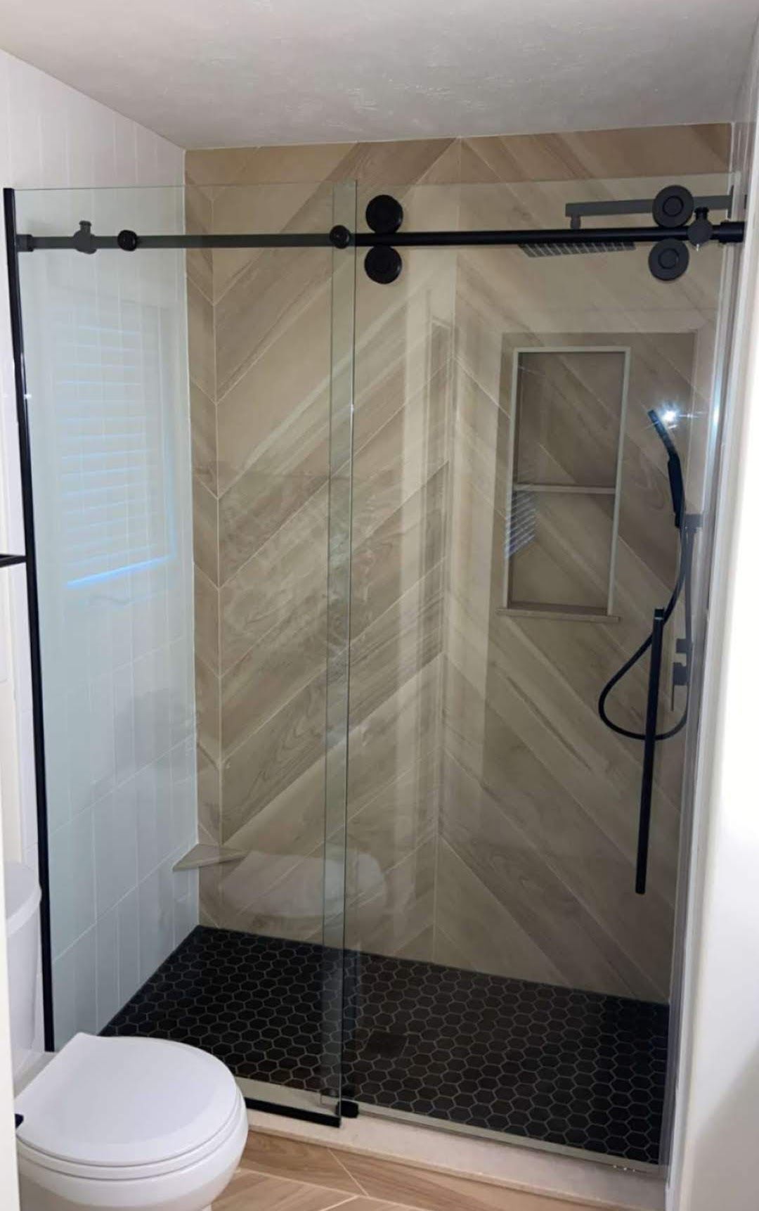 Modern bathroom with gray tile, toilet, sink, and window with blinds.