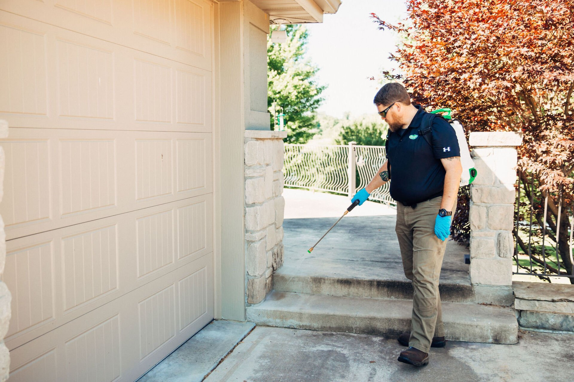 Man spraying eaves of a beige house with a handheld sprayer outdoors