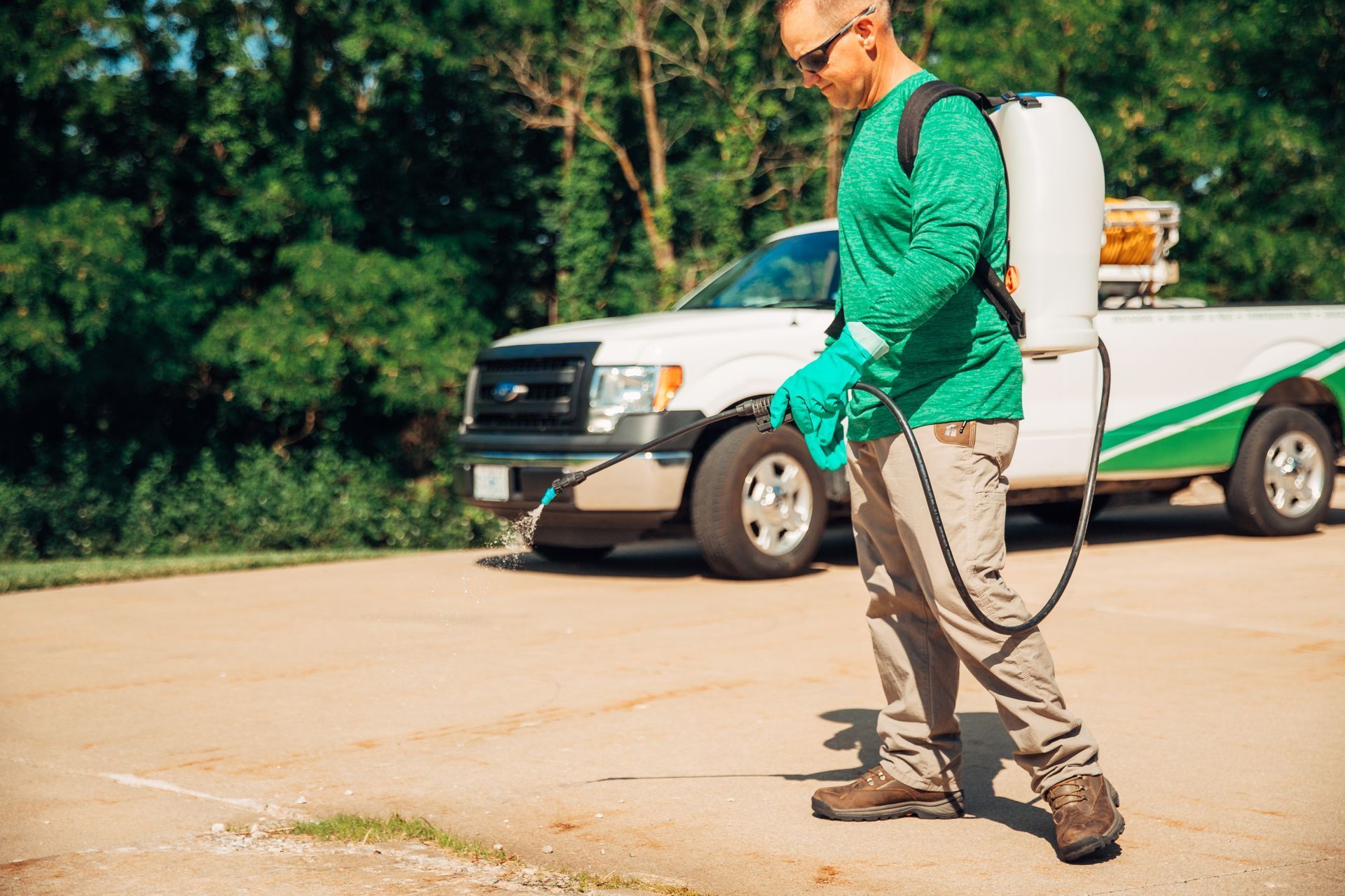 Worker spraying pesticide beside a white service truck on a driveway