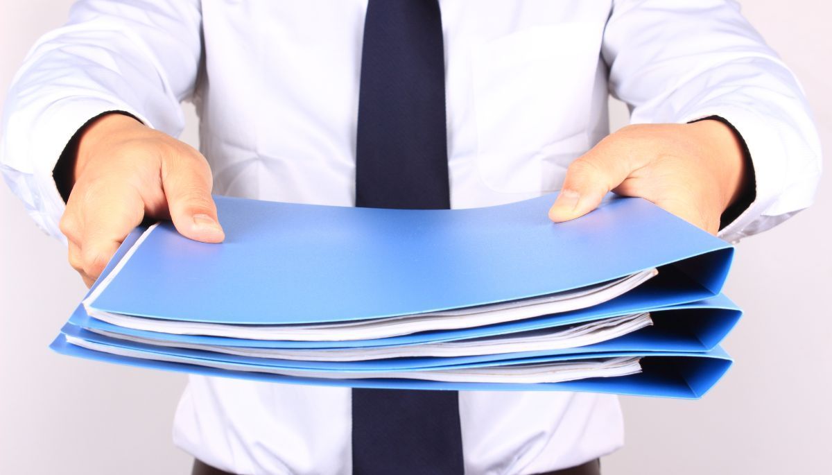 Person in a white shirt and tie holding a stack of blue file folders