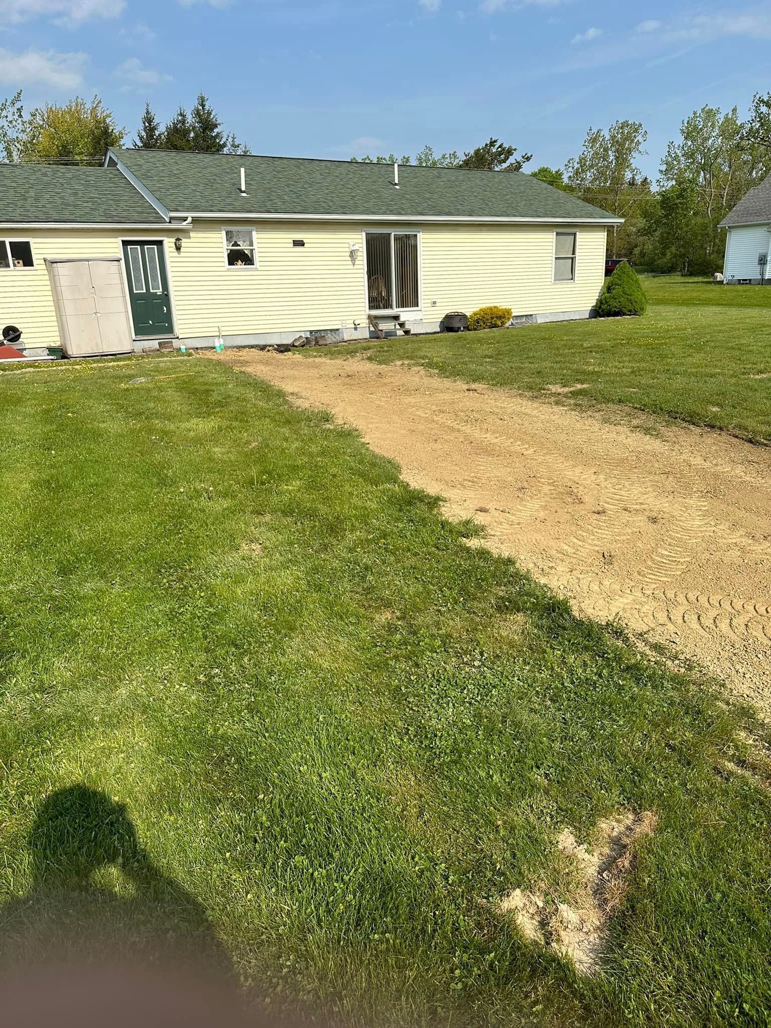 A gravel path leads to a light yellow house with a green roof, set in a grassy yard under a blue sky.