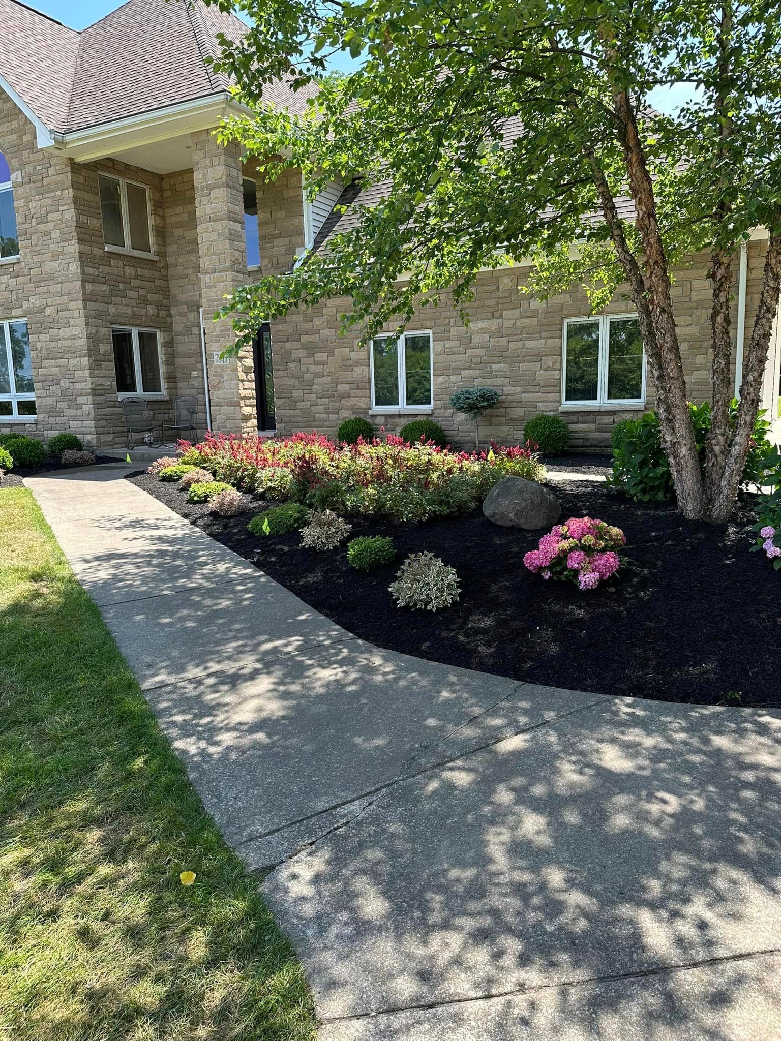 Stone facade house with flower beds and a curved walkway.