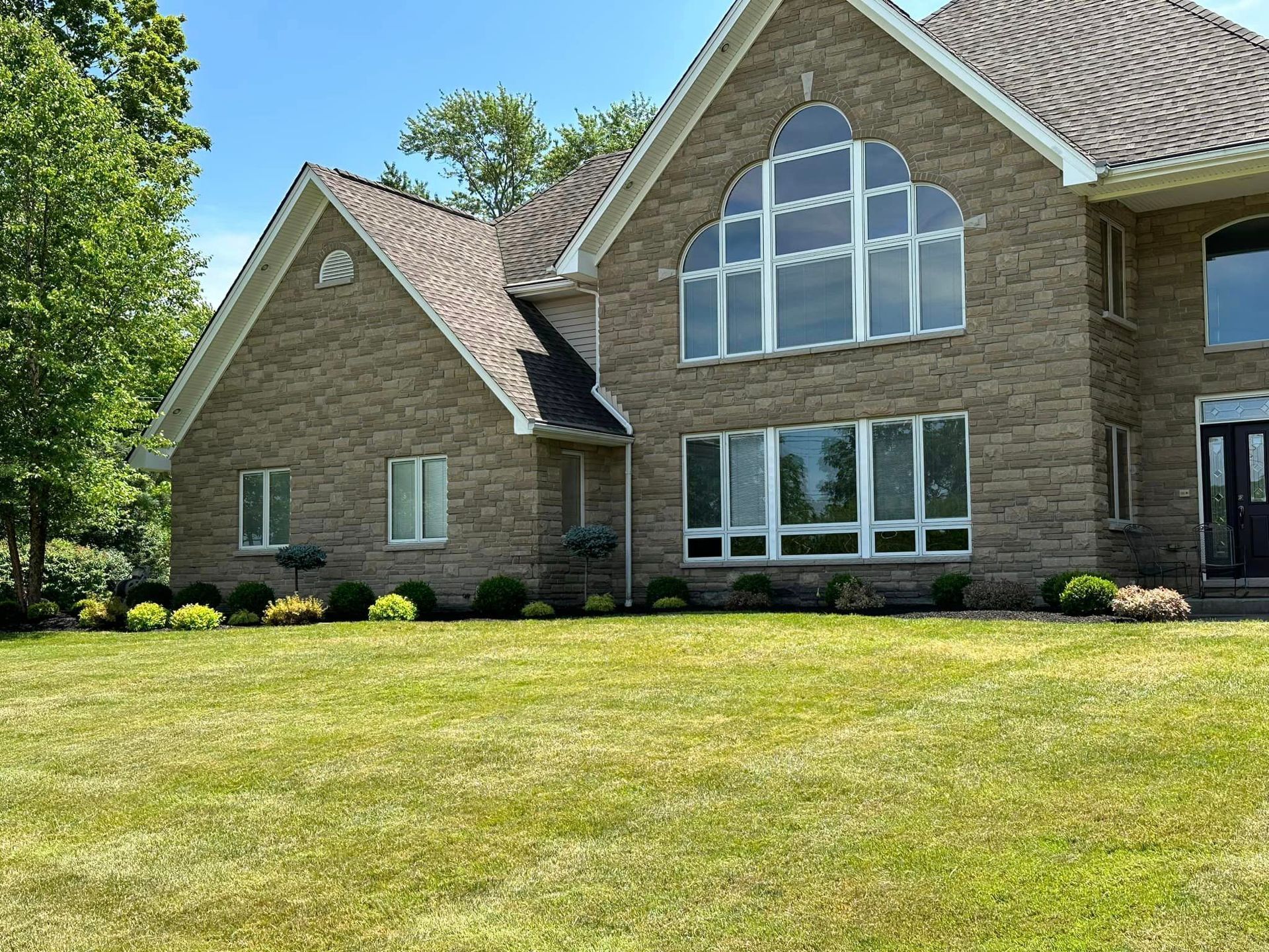 Two-story brick house with a well-manicured lawn and landscaping on a sunny day.