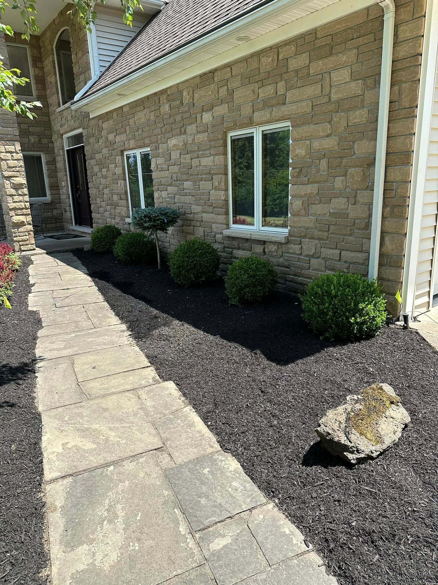 Stone house exterior with a paved walkway and landscaped black mulch beds.