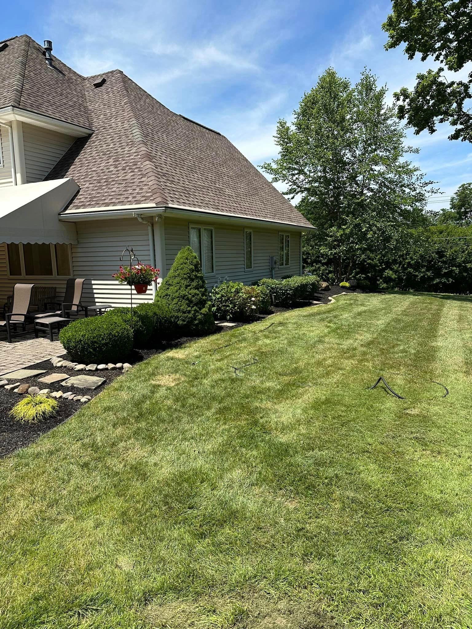 Backyard with manicured lawn, house with textured roof, green bushes, and a partly cloudy sky.