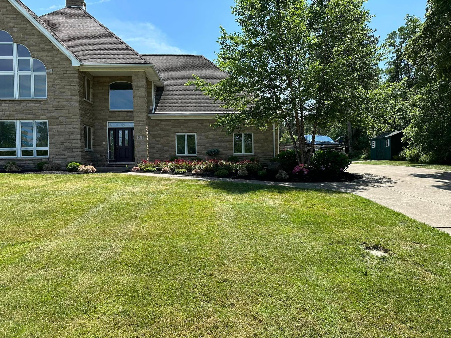 Large stone house with a manicured lawn and garden under a bright blue sky.