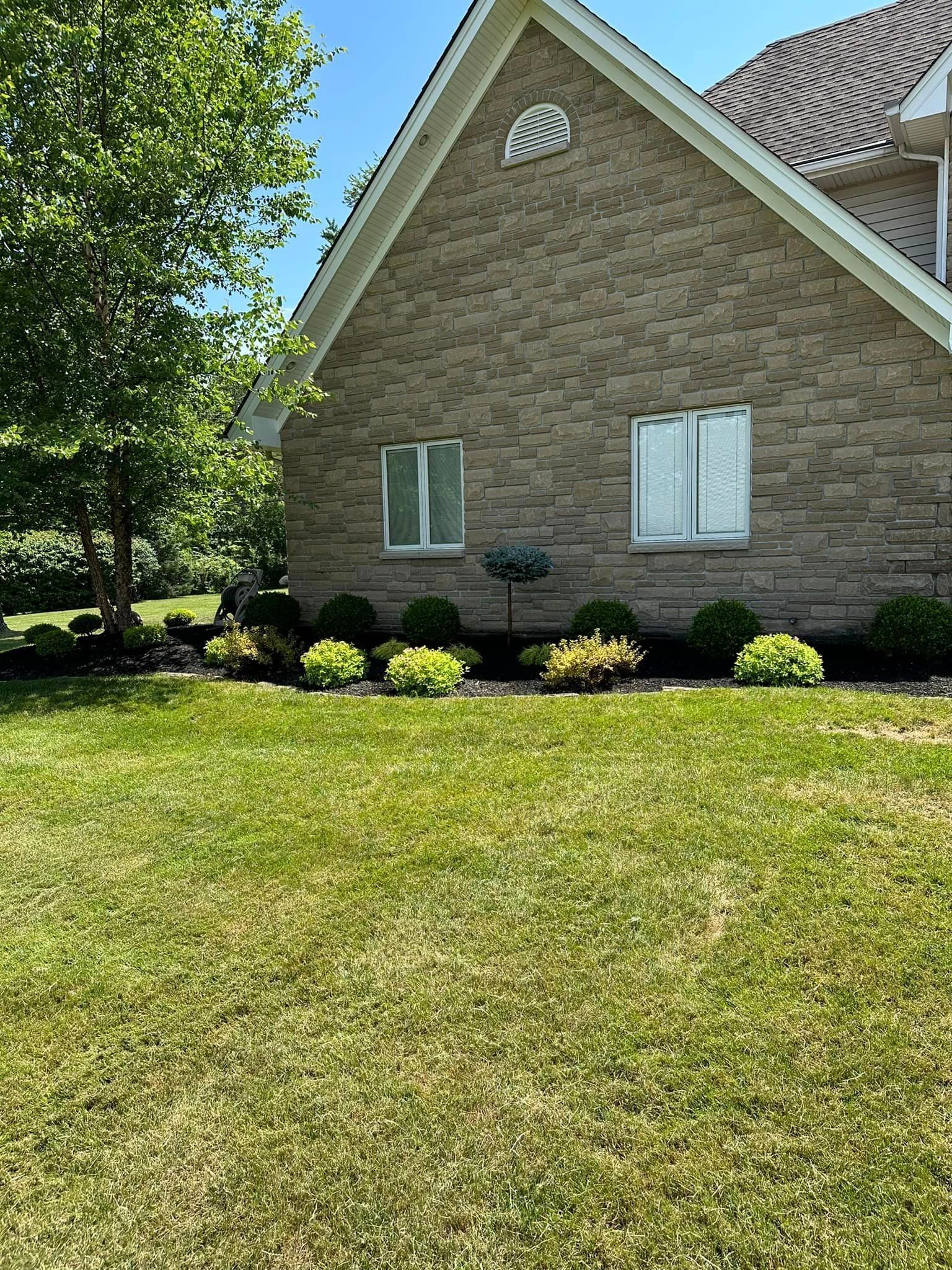 House with brick facade, two windows, and manicured landscaping in front of lawn.