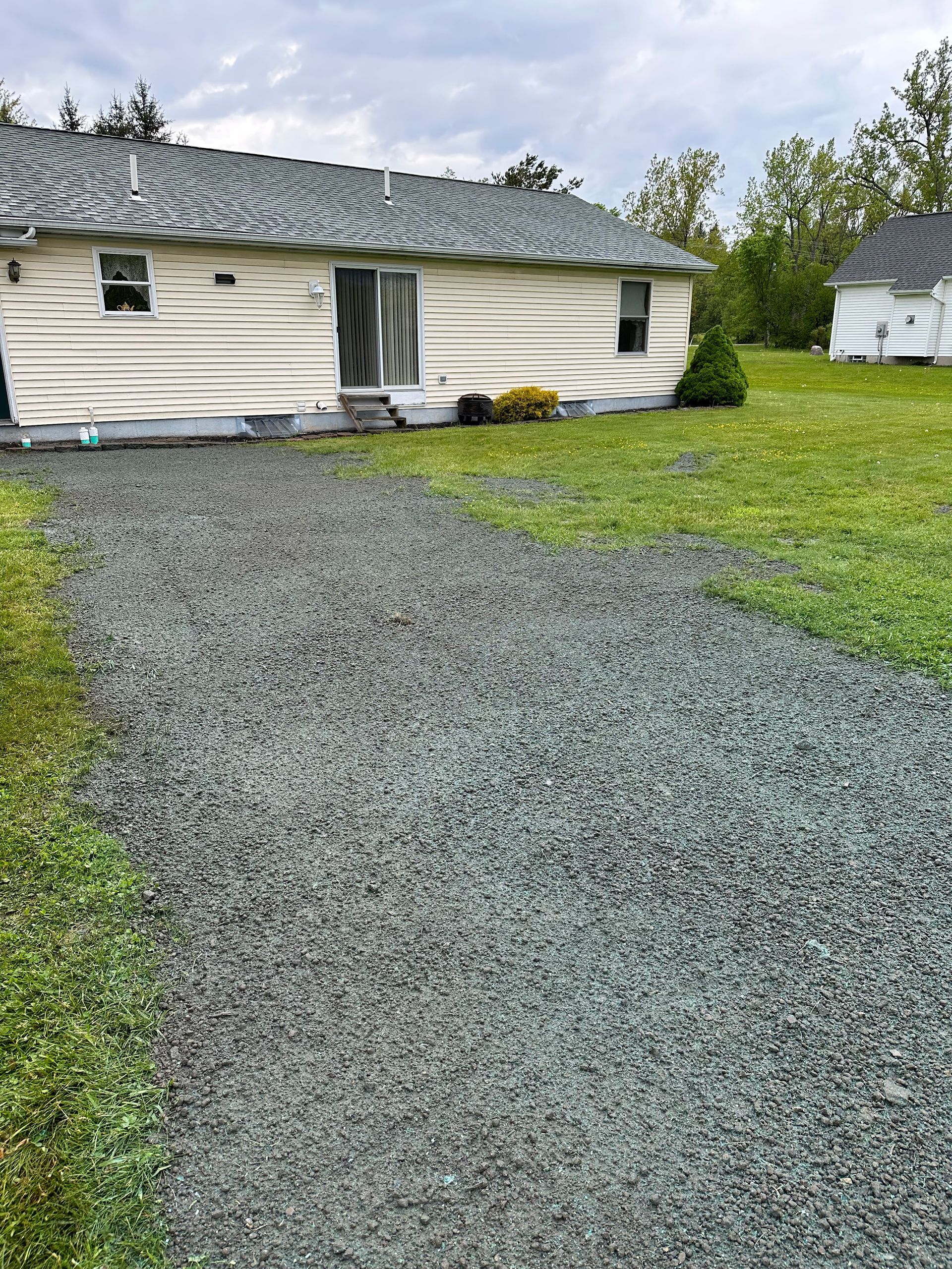 Gravel driveway leading to a white-sided house with a sliding glass door and small front lawn.