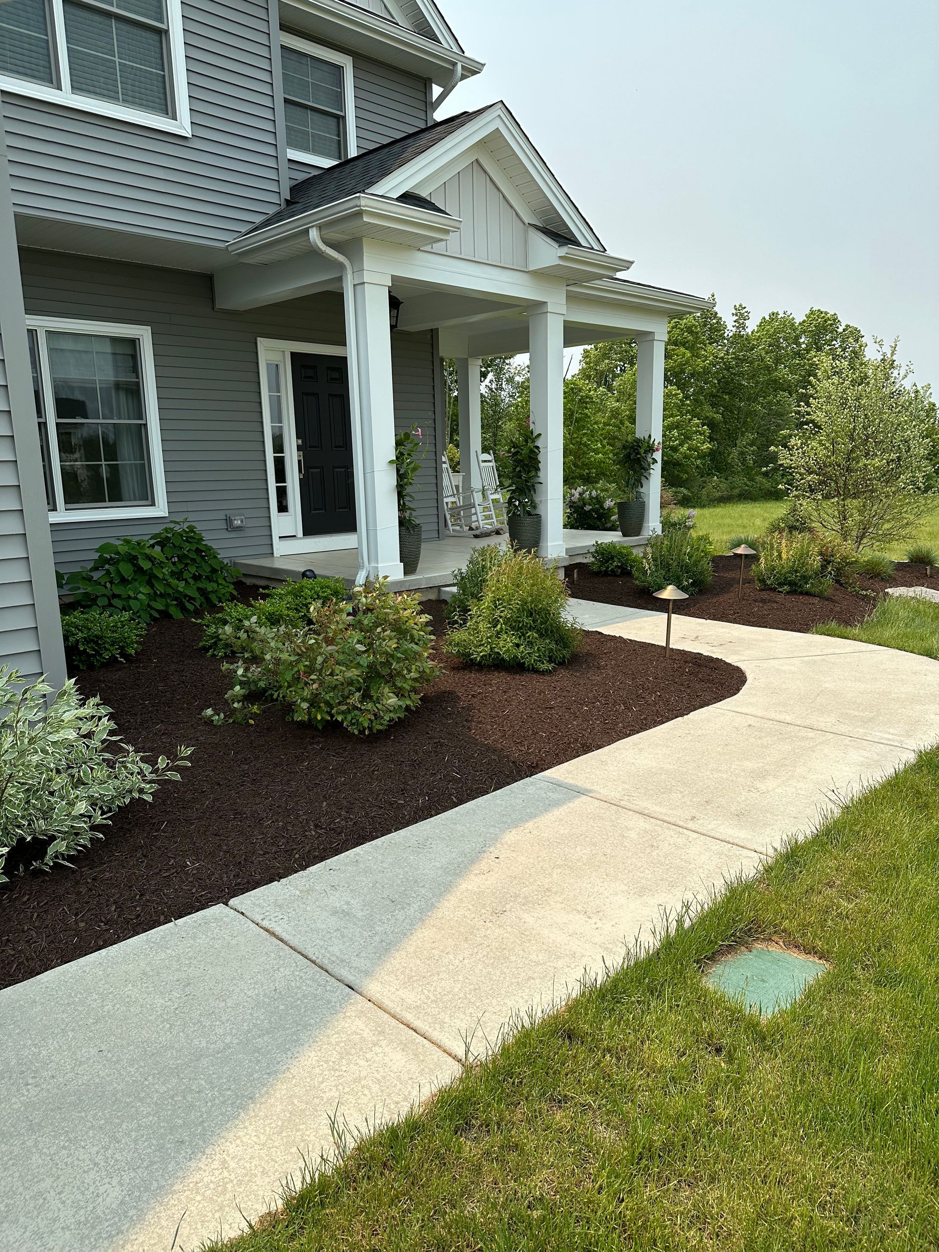 Gray house with a front porch, a curved walkway, and landscaping with brown mulch.