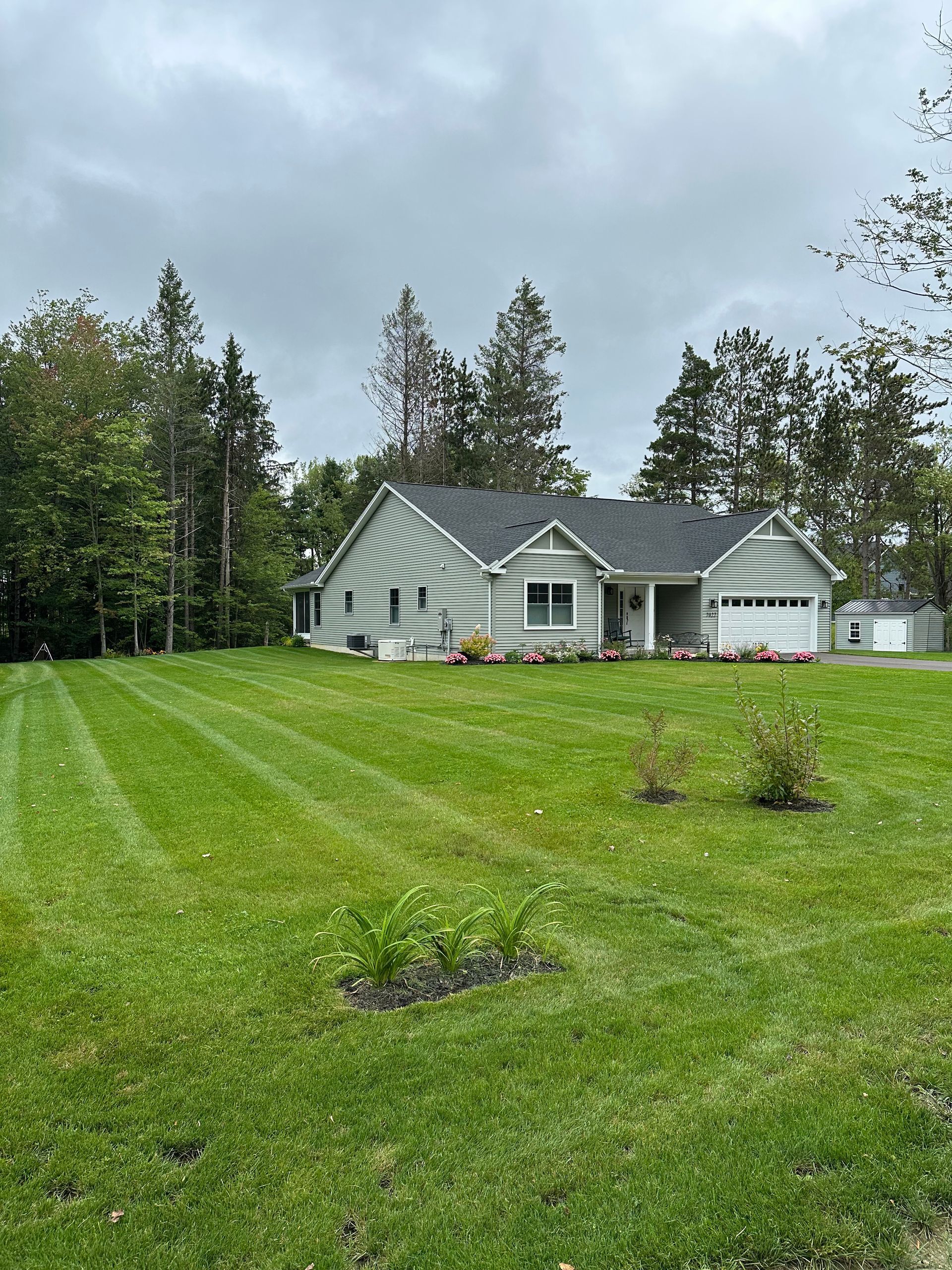 Light green house with a dark gray roof on a large lawn with freshly cut grass.