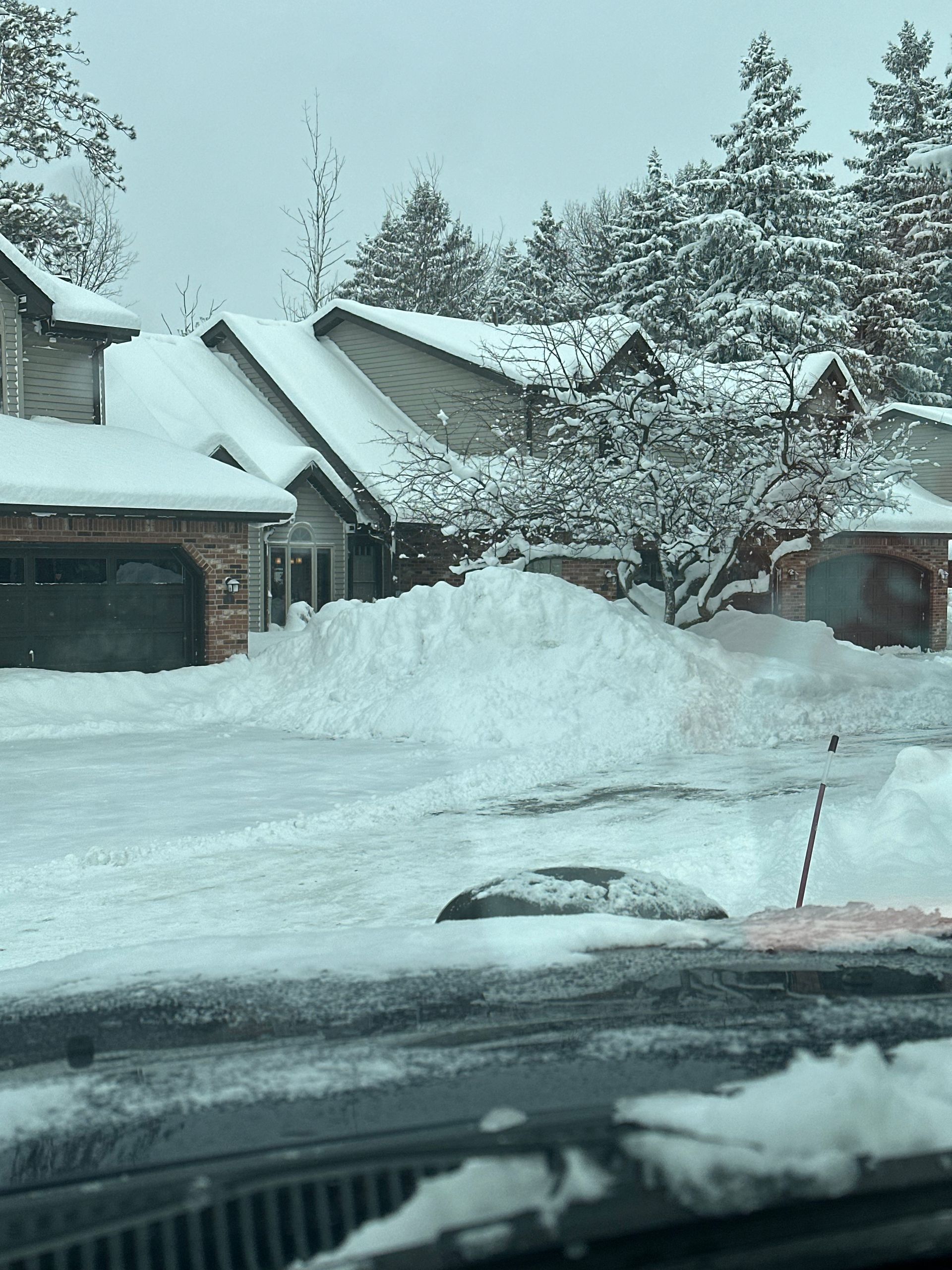 Snow-covered houses and driveway after a snowfall. Pile of snow obscures the front of the home, winter scene.