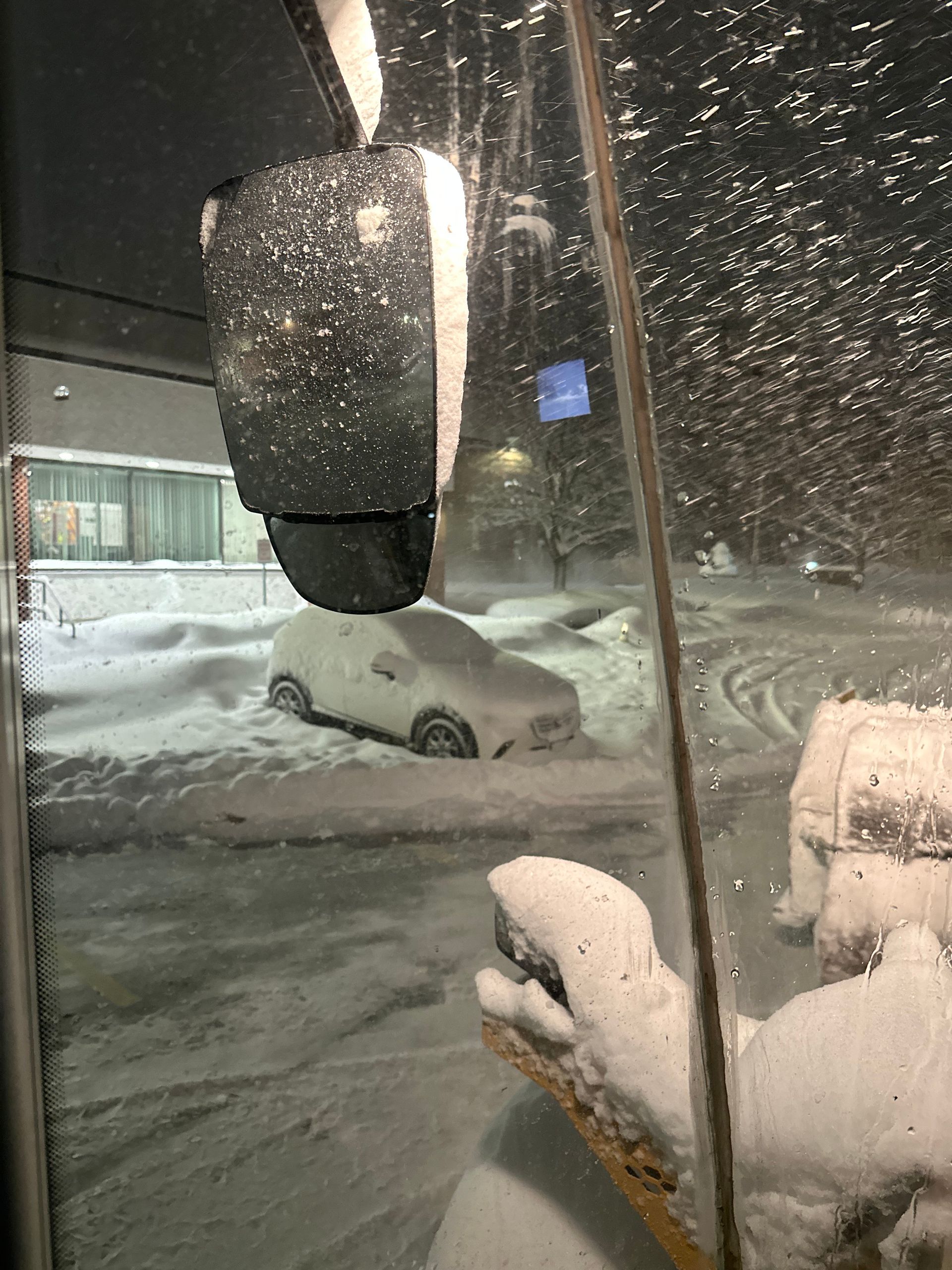 Snowy scene: a car buried in snow, viewed from inside. Dark night.