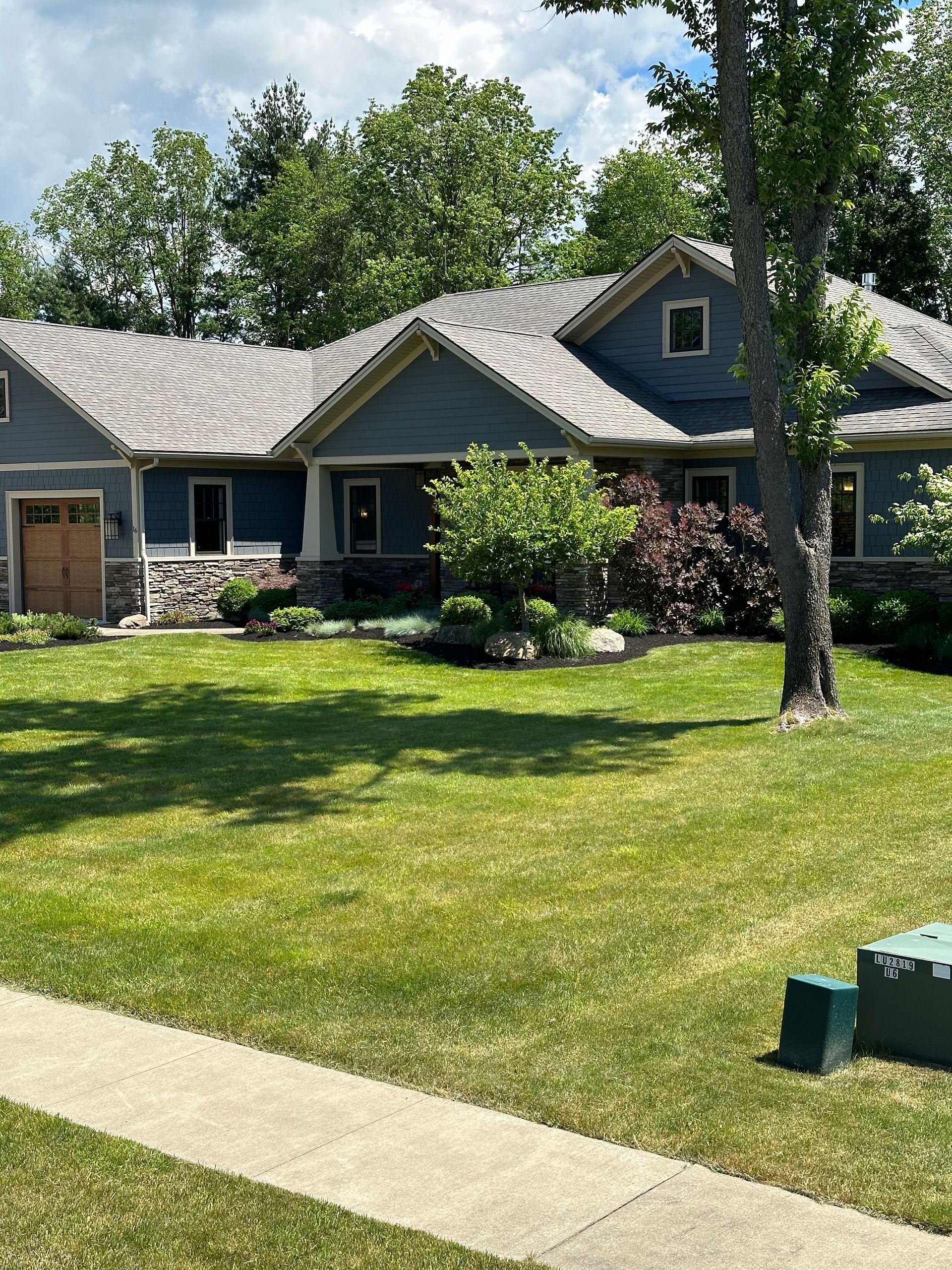 Blue house with gray roof, stone accents, and green lawn.