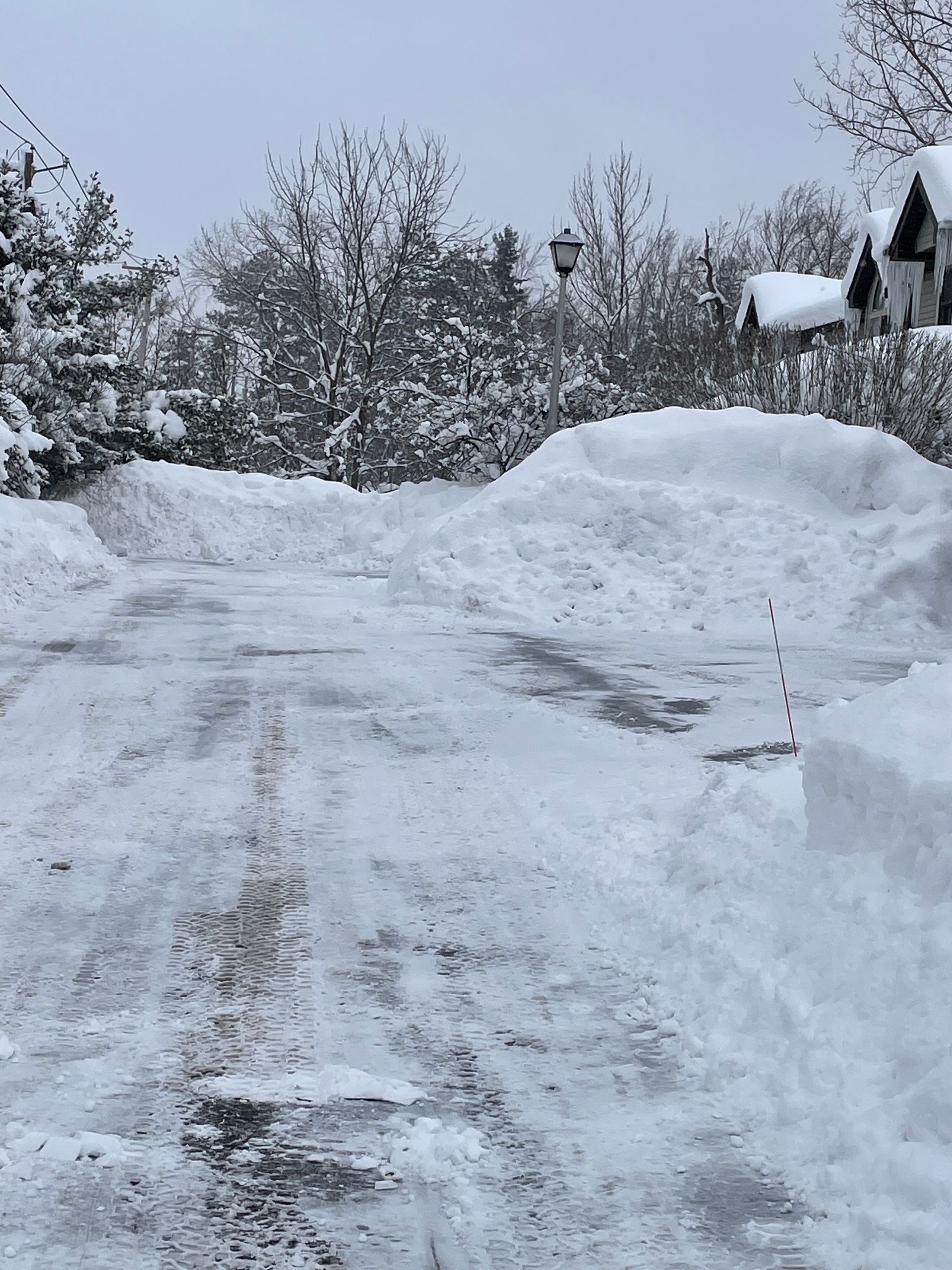 Snow-covered road with high snow banks on either side. Cloudy day in a residential area.