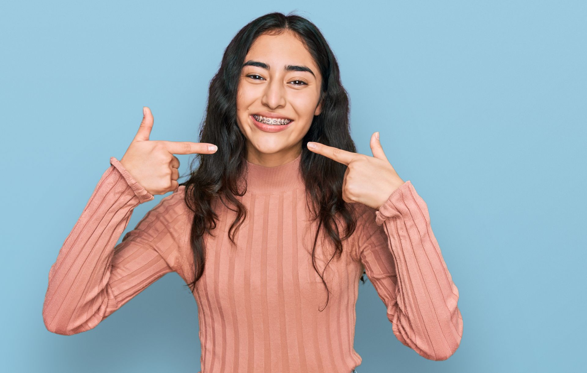 A girl with dental braces, wearing casual clothes, cheerfully showing and pointing at her mouth. A girl with dental braces, wearing casual clothes, cheerfully showing and pointing at her mouth.
