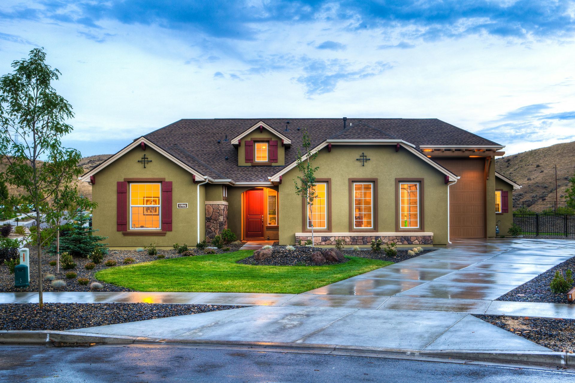 Modern single-story house at dusk with lit windows, red front door, and a wet driveway