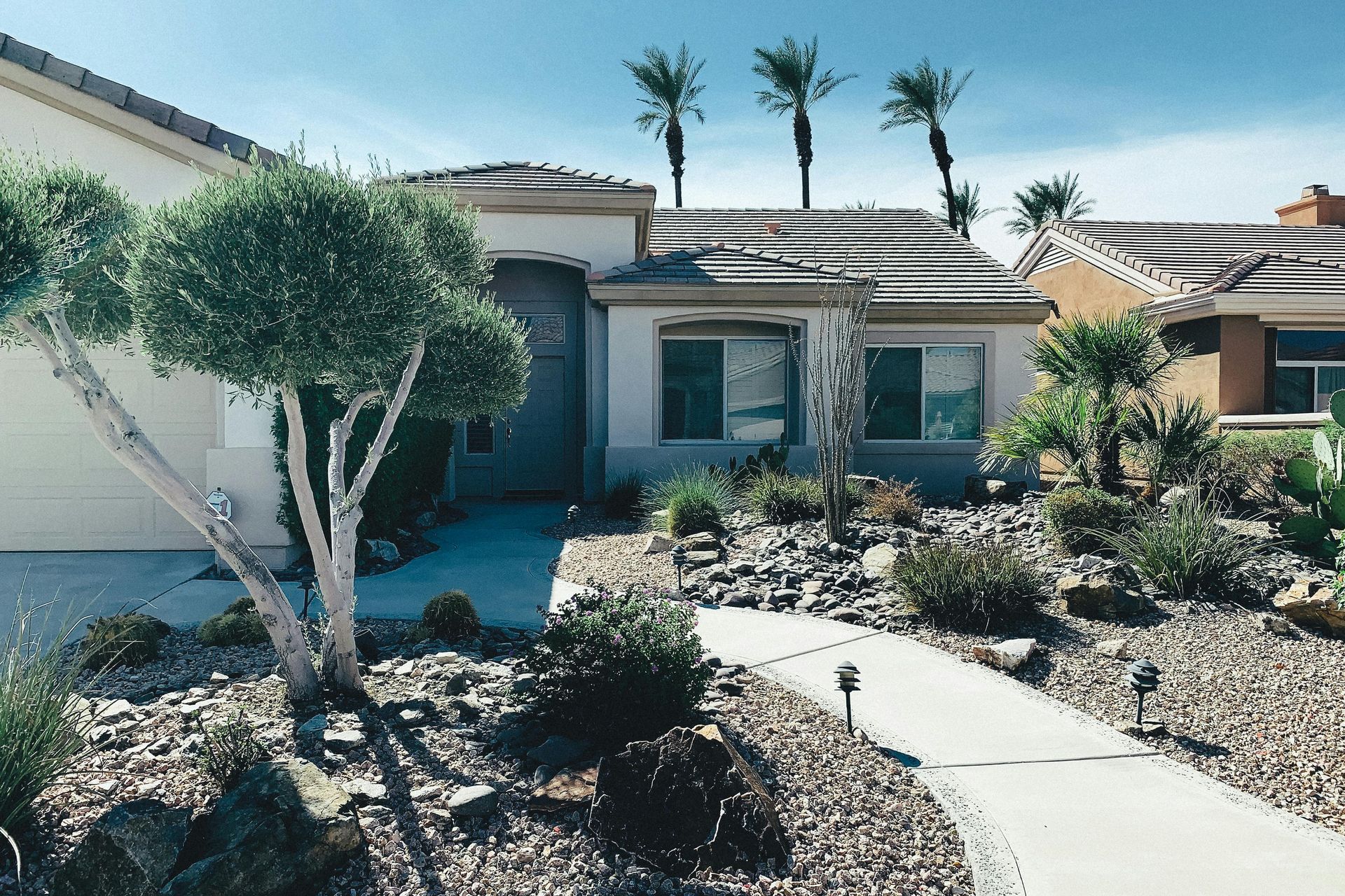 Rustic wooden house with red roof, front steps, and desert plants in a sunny yard