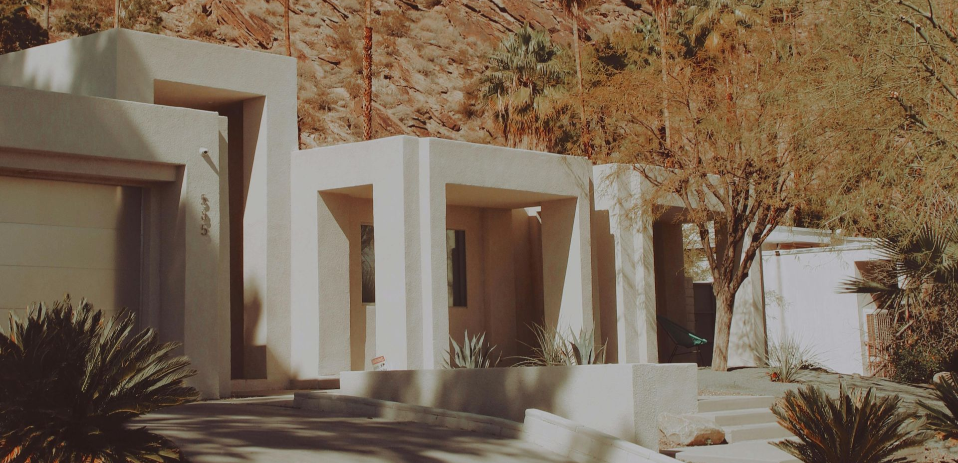Modern white stucco building with shaded entryways and desert landscaping with palm trees