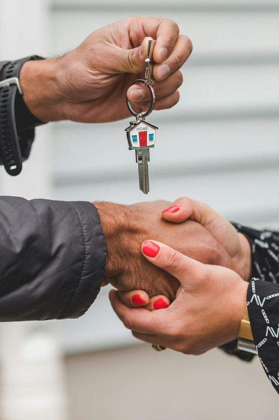 Hands exchanging a keychain with a house key, over a handshake.