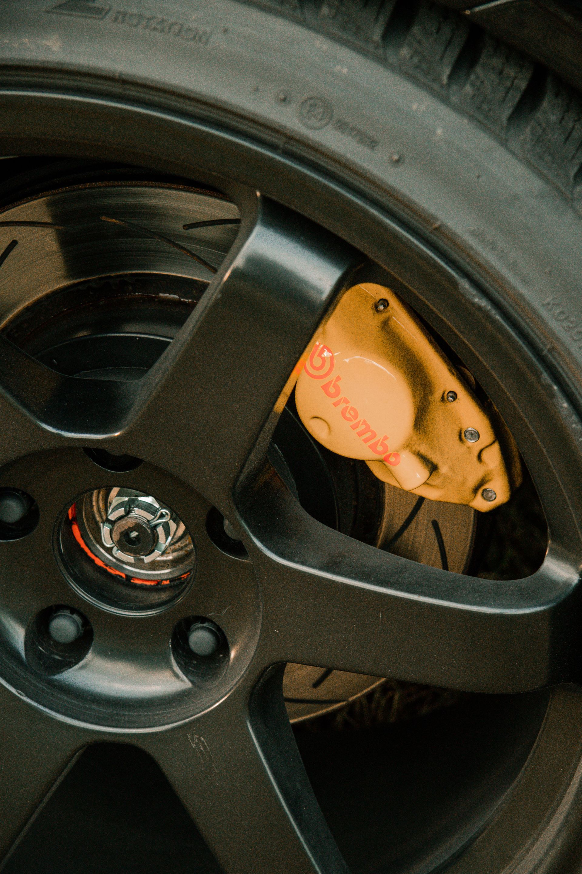 Close-up of a black car wheel with an orange brake caliper behind the rim
