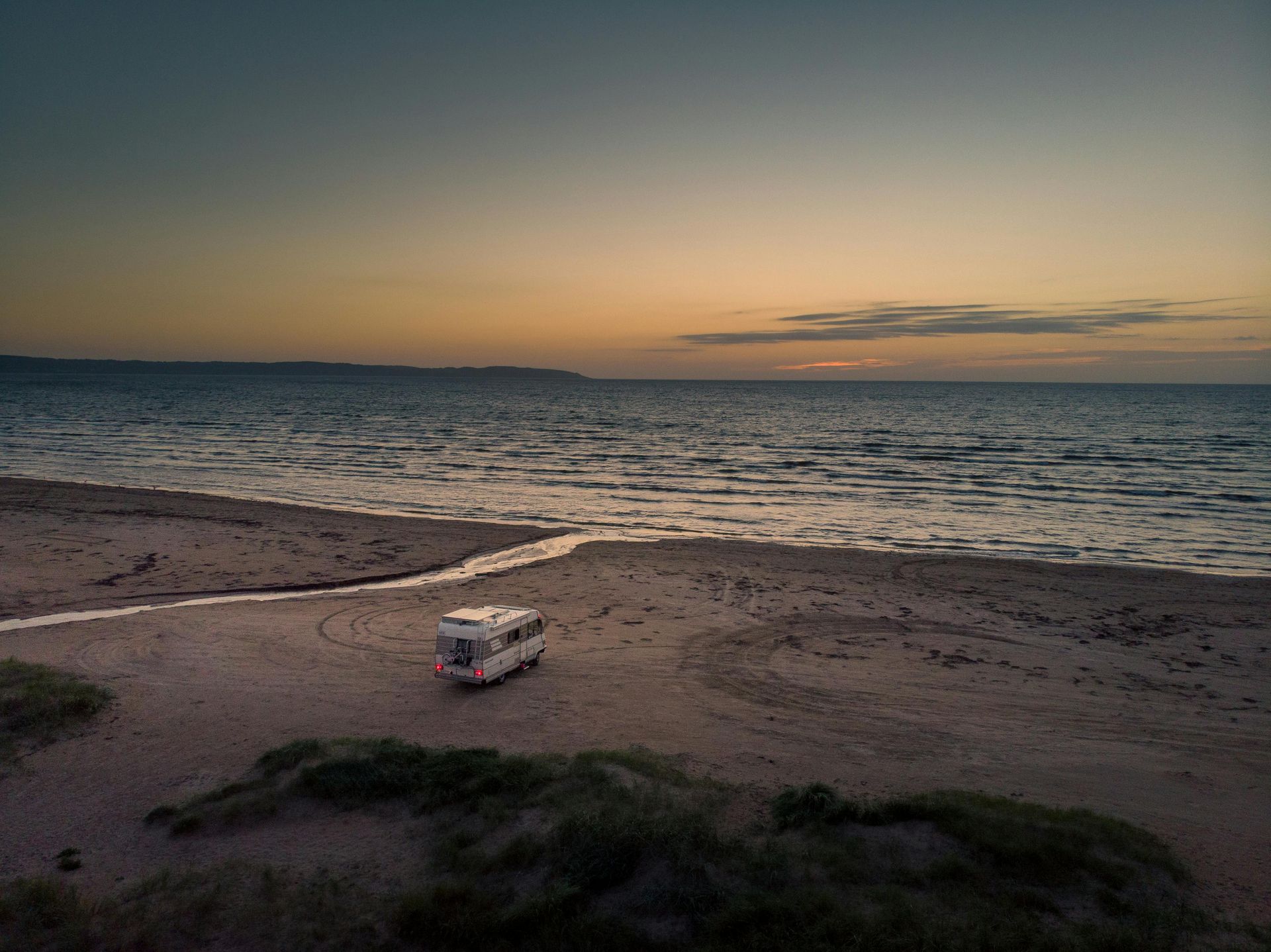 A camper van parked on a sandy beach at sunset, with ocean waves in the background.
