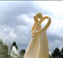 A statue of a bride and groom kissing in front of a cloudy sky.