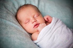 Sleeping newborn wrapped in a white blanket, resting on a soft blue-gray blanket