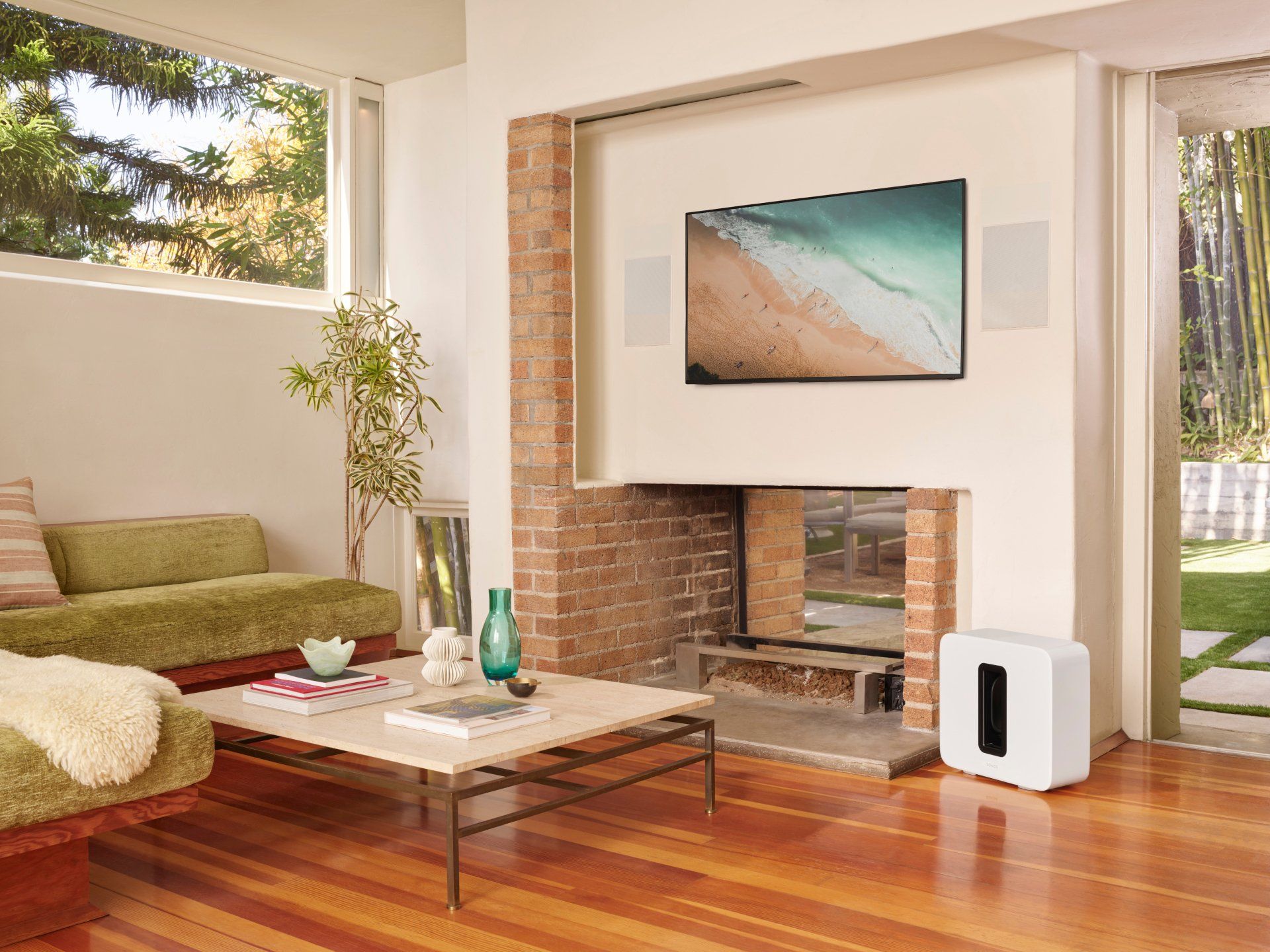 Living room with TV, speakers, couch, coffee table, and subwoofer, with a view of trees and greenery.