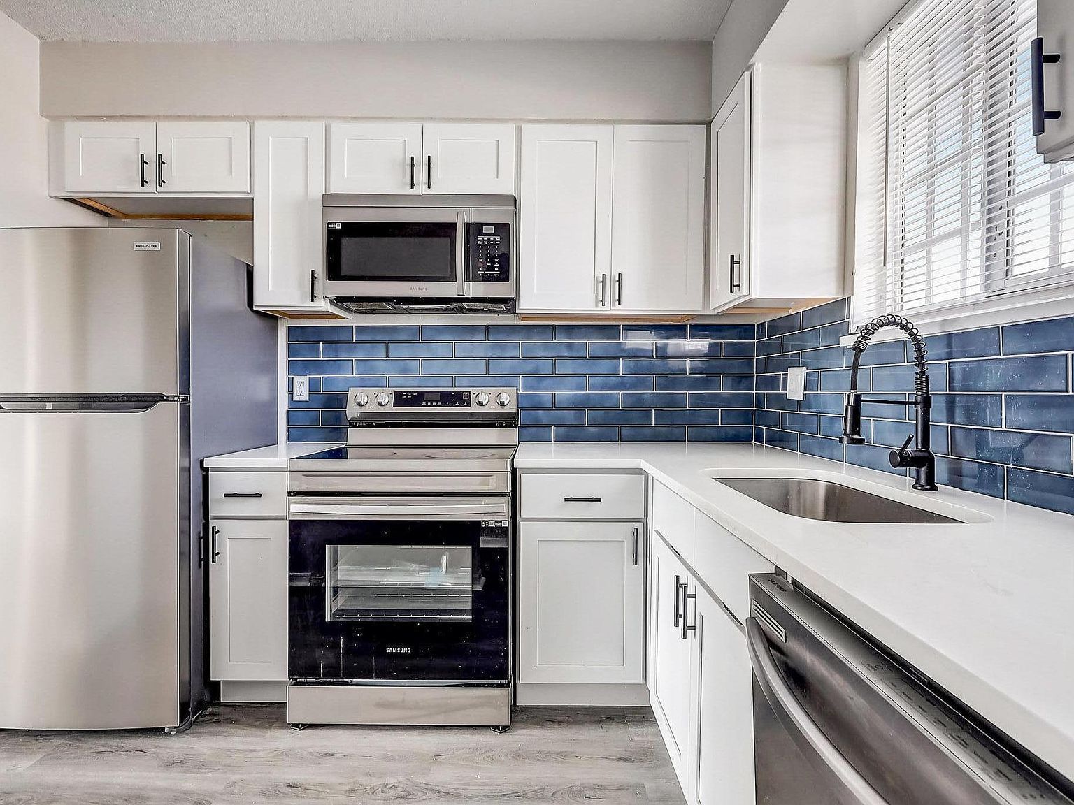 Modern white kitchen with stainless appliances and blue tile backsplash