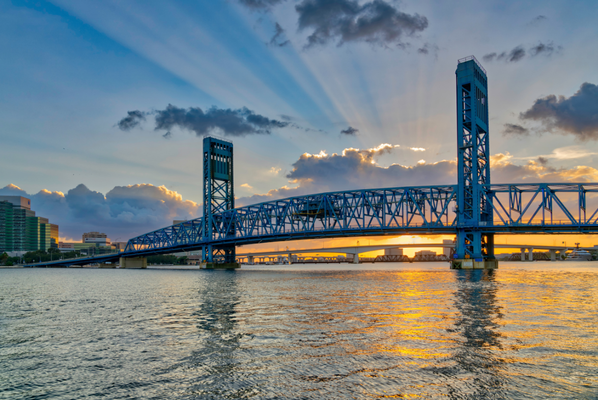 Blue bridge over a river at sunset, with clouds and reflections on the water