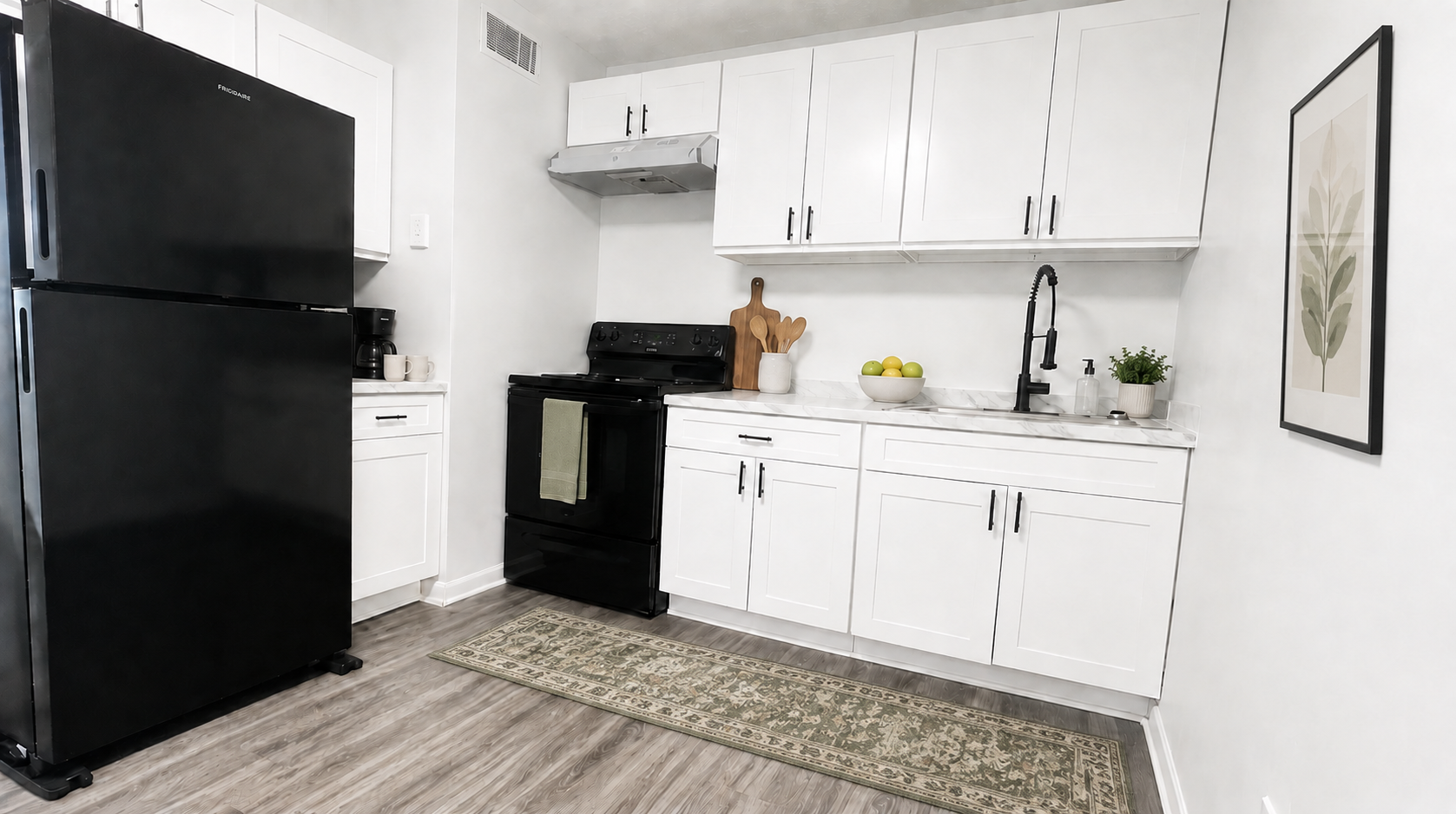 Bright white kitchen with black refrigerator, stove, cabinets, and patterned rug on the floor.