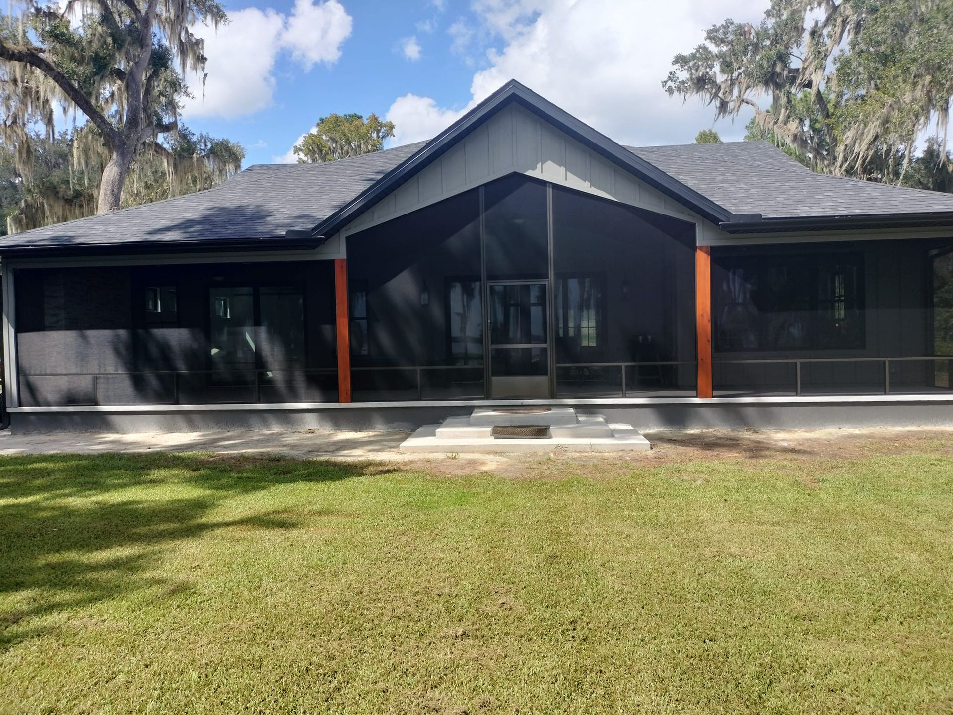 A house with a screened in porch and a large lawn in front of it.