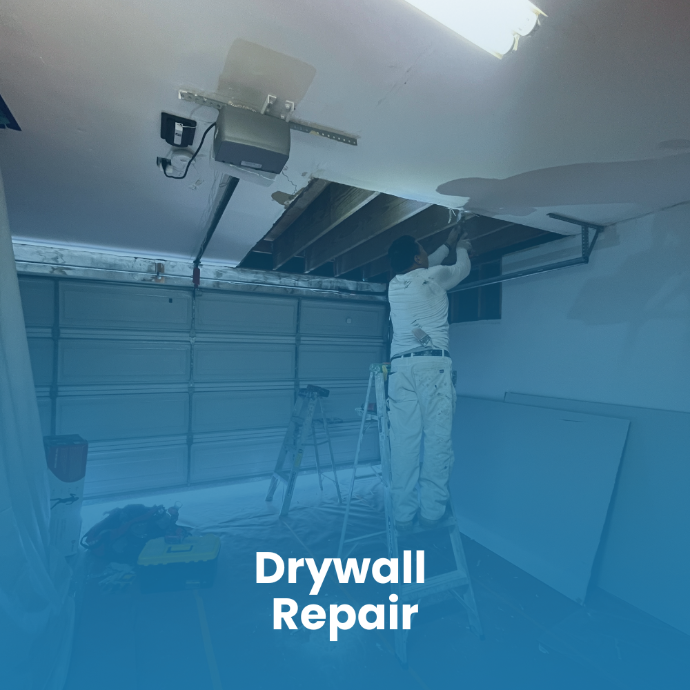 A person on a ladder repairs a hole in a garage ceiling, surrounded by tools and construction materials.